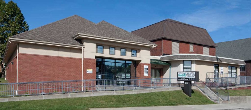 Cropped, parking lot view of New Castle Primary Care entrance showing access ramp