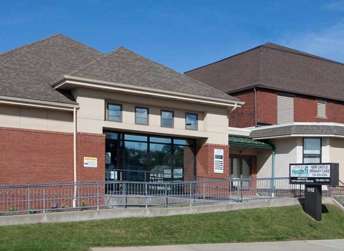 Cropped, parking lot view of New Castle Primary Care entrance showing access ramp