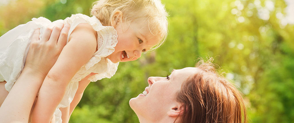 A woman holds a toddler above her head. They smile at each other