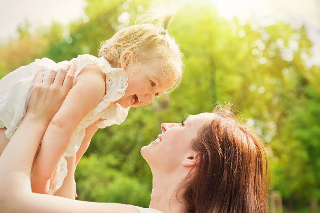 A woman holds a toddler above her head. They smile at each other