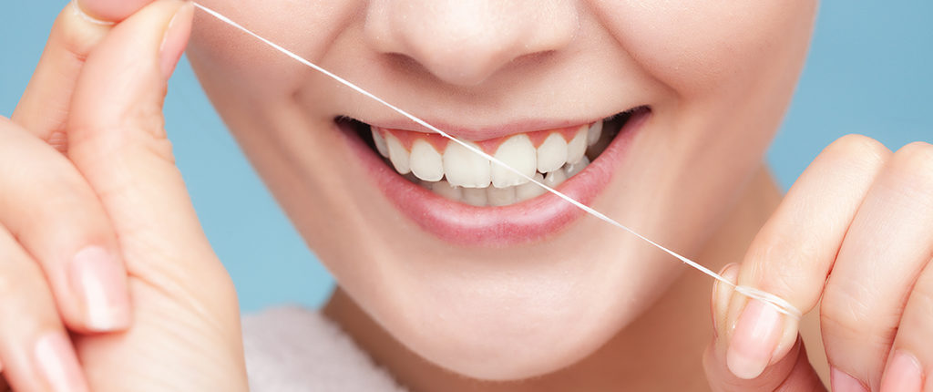 A light-skinned woman with a white smile holds dental floss close in front of her mouth