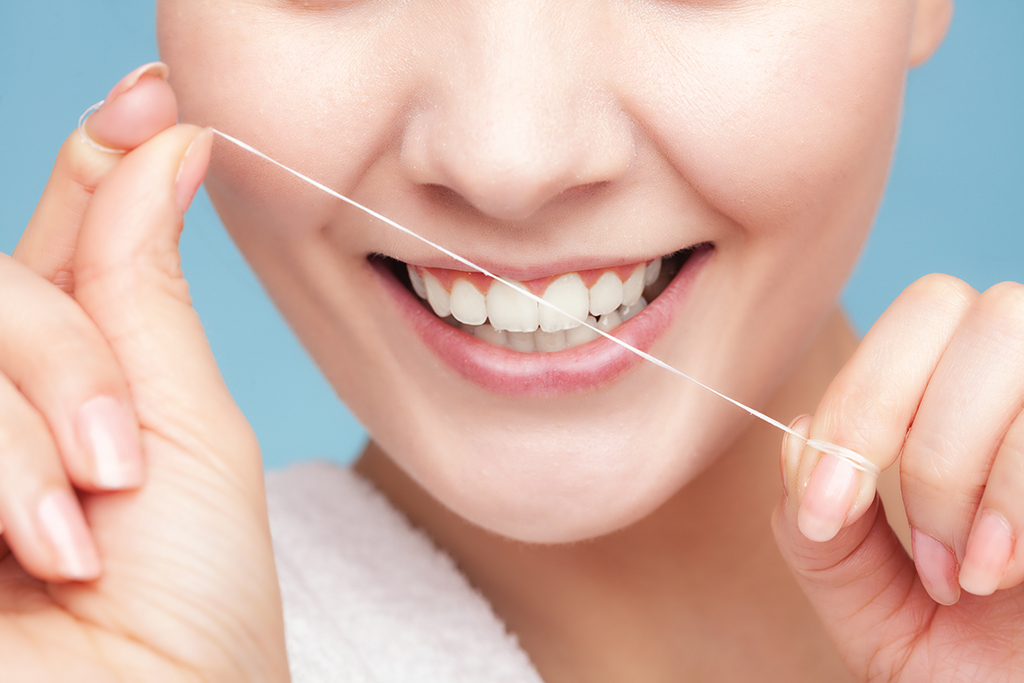 A light-skinned woman with a white smile holds dental floss close in front of her mouth