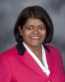 Portrait of a smiling woman wearing a pink jacket with a black collar over a white shirt