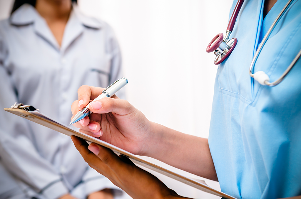 A close-up of a medical professional writing on a clipboard with a silver pen