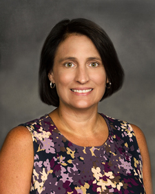 A woman with short black hair, earrings, and a flower patterned shirt