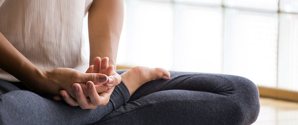 A woman sits in half lotus position on a yoga mat, her face is cropped out of the photo