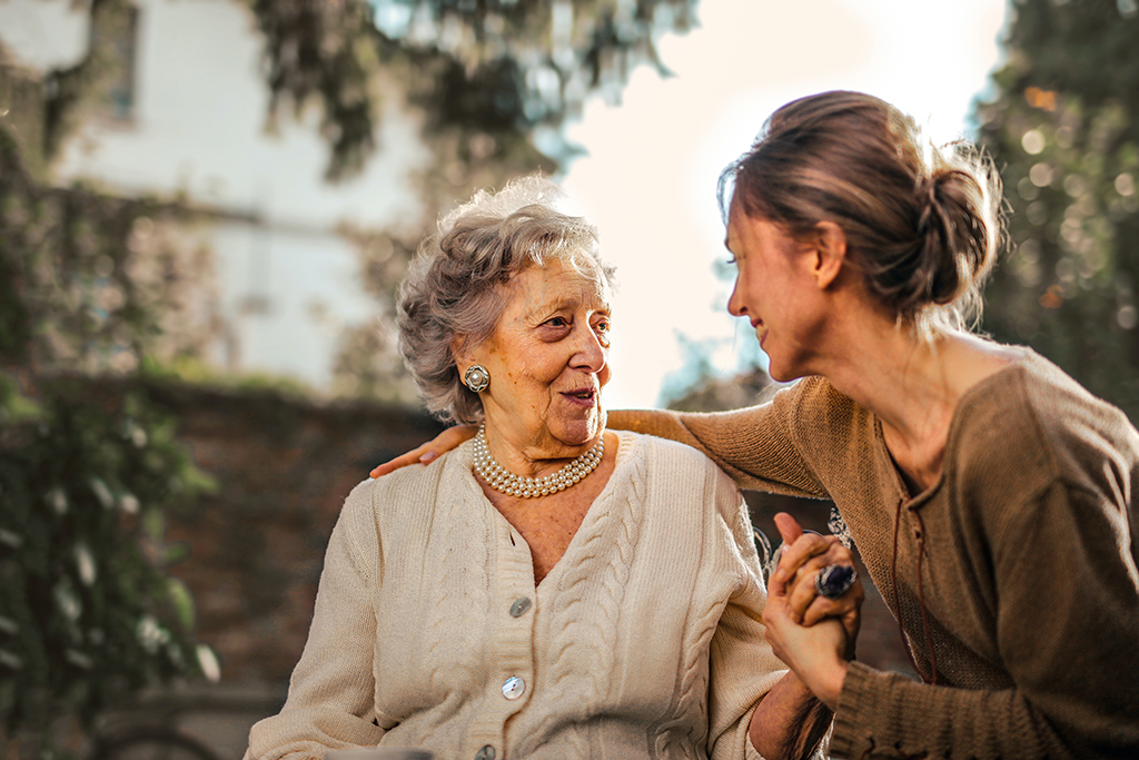 A younger woman has her arm around an older woman's shoulders, they are looking at each other