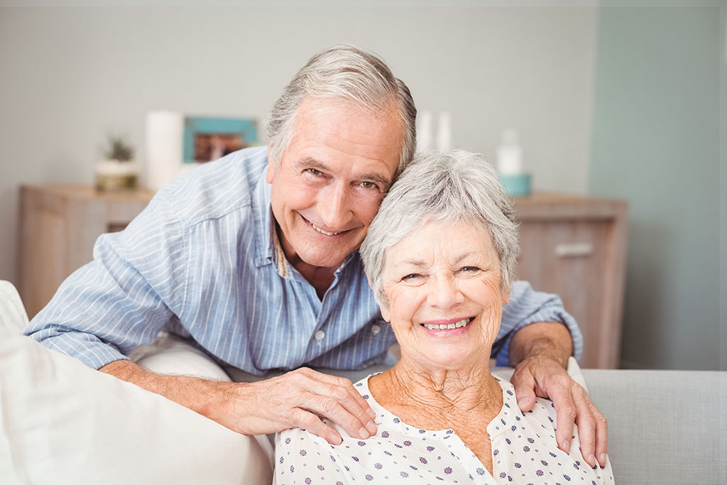 A man leans over a couch to pose with a woman who is seated, his hands are on her shoulders