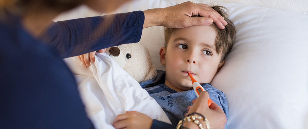 Young boy in a bed getting his temperature checked with an oral thermometer