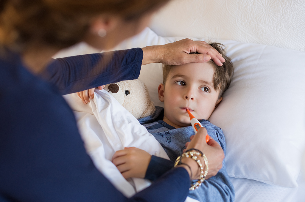 Young boy in a bed getting his temperature checked with an oral thermometer