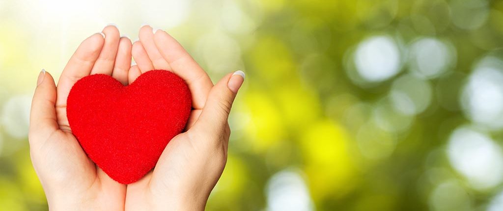 A woman's hands hold a red fabric heart, the background is distorted