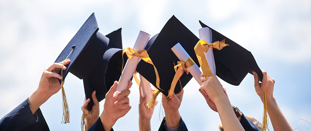 A close-up of hands holding mortar boards and diplomas