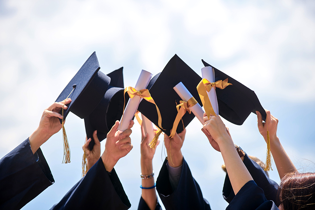 A close-up of hands holding mortar boards and diplomas