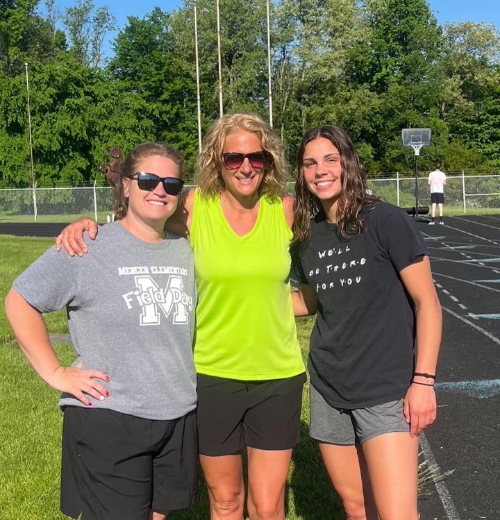 Three women in activewear pose next to a track. Two of the three women have sunglasses on