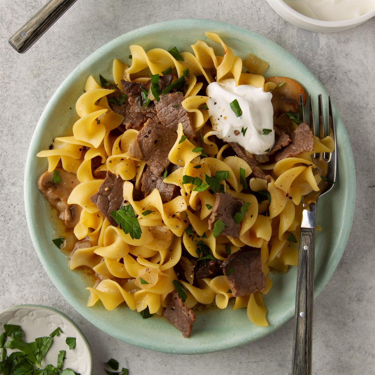 Top-down of a pale green dish with corkscrew noodles, cooked beef chunks, and mushroom slices.