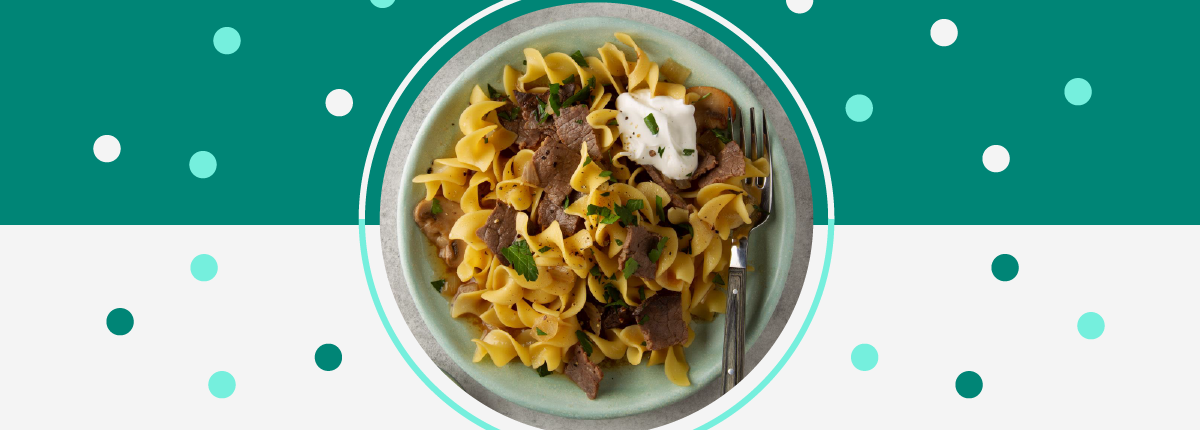 Beef stroganoff bowl with beef slices, egg noodles, mushroom sauce, parsley, and sour cream dollop