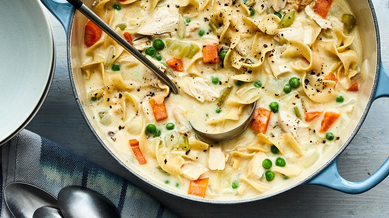 A pot full of chicken noodle soup with a ladle partially submerged