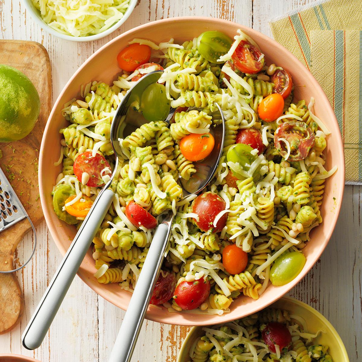 Top-down of spiral pasta noodles with cherry tomatoes and avocado sauce in a pale red bowl