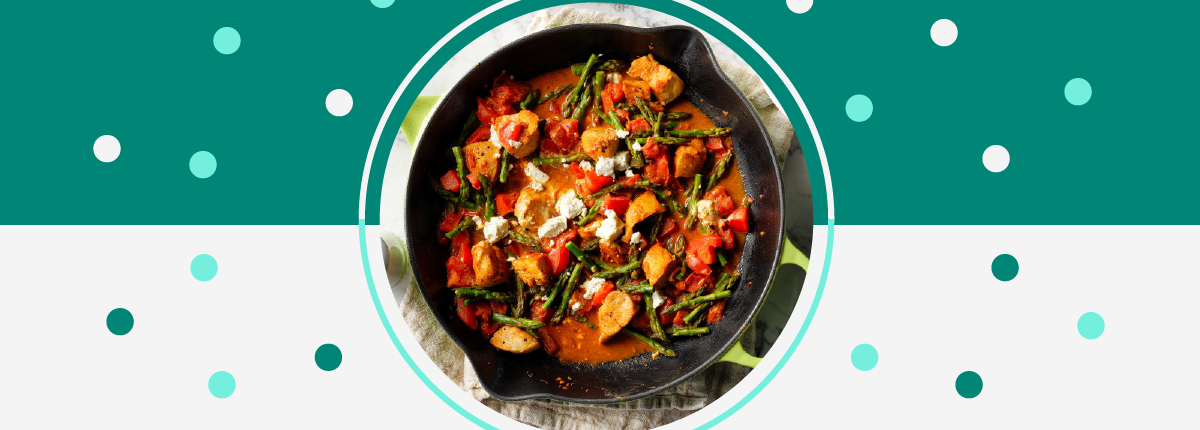 Cooked chicken, tomatoes, asparagus, and goat cheese in red sauce in a cast iron pan