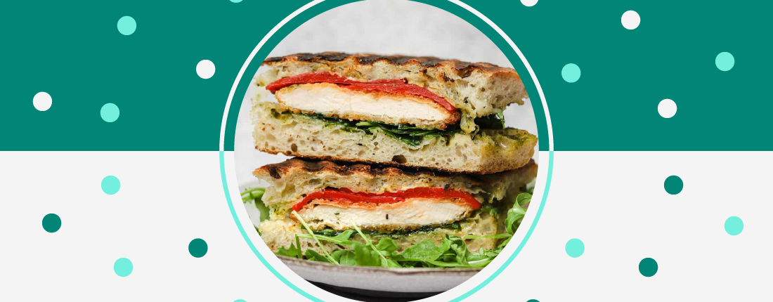 Two halves of a grilled chicken panini with tomato and greens stacked on top of each other