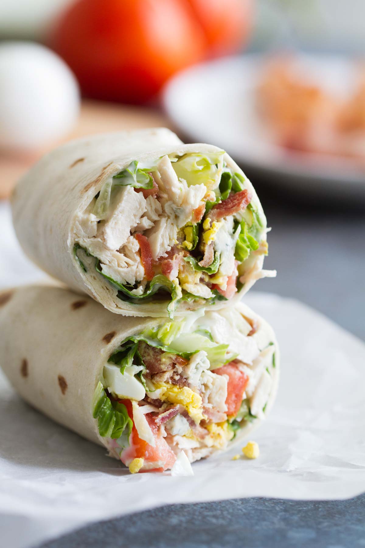 Close-up, two halves of a wrap filled with lettuce, chicken, bacon, tomato, and hardboiled egg