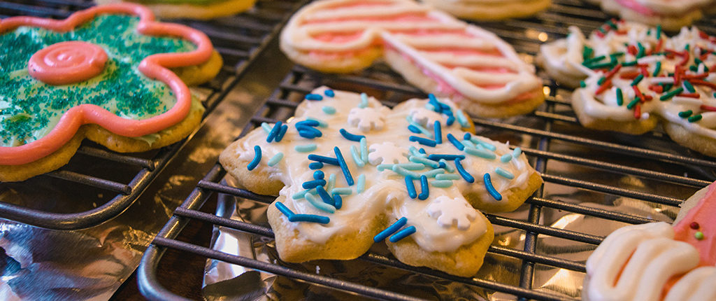 Close-up as sugar cookies cool on racks, cut into Christmas shapes, decorated with colored frosting.