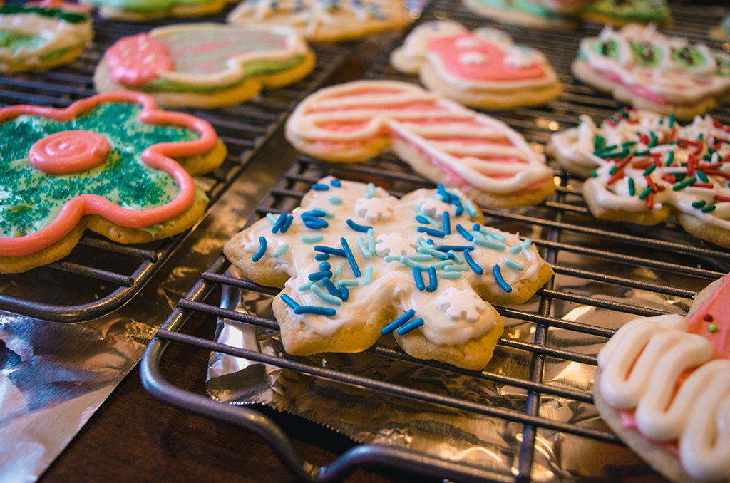 Close-up as sugar cookies cool on racks, cut into Christmas shapes, decorated with colored frosting.
