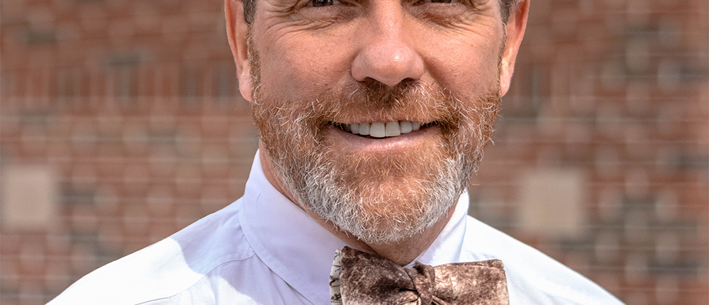 A close-up of a man's nose, mouth, and bearded chin. The man is wearing a white shirt and bow tie