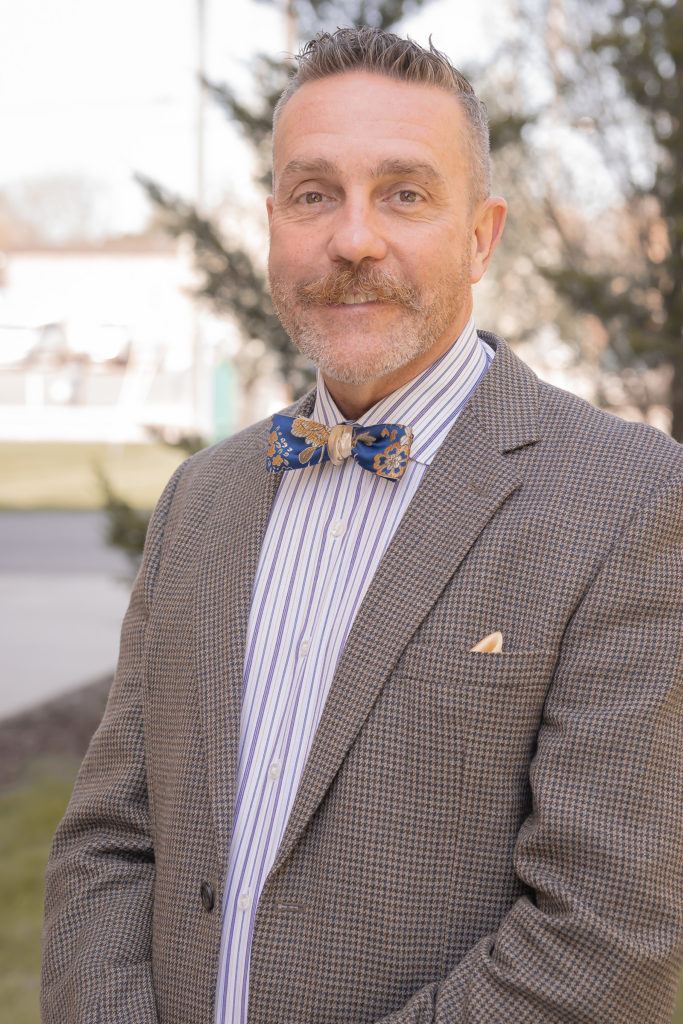 Dr. Garrow in a blazer, striped shirt, and bow tie, poses for a picture outside