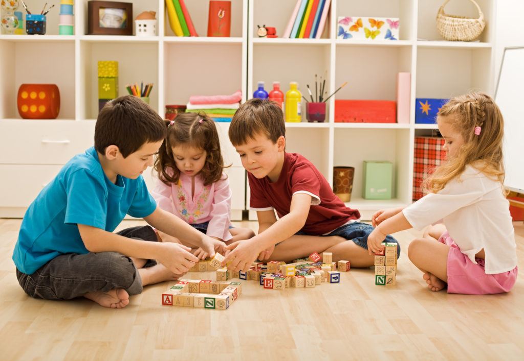 Group of four kids playing with building blocks in a playroom.
