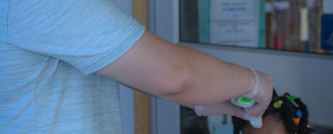 A man wearing a surgical mask uses a forehead thermometer on a young girl