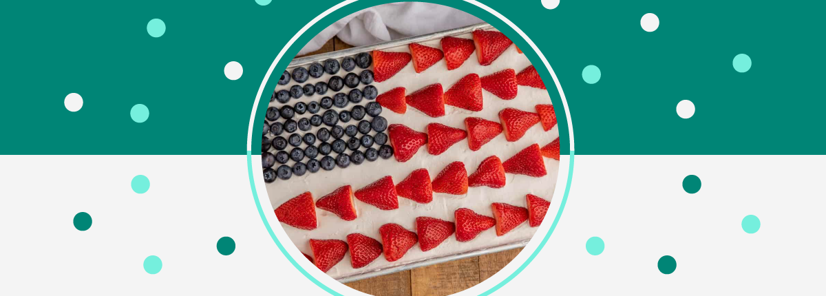 White-frosted cake decorated like the US flag with strawberries as stripes, blueberries as stars