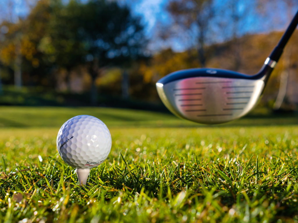 An extreme close-up of a golf ball on a tee, with a driver's club head in the immediate background
