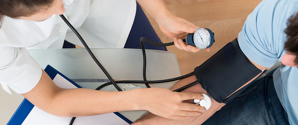 A medical professional uses a stethoscope to check a man's blood pressure