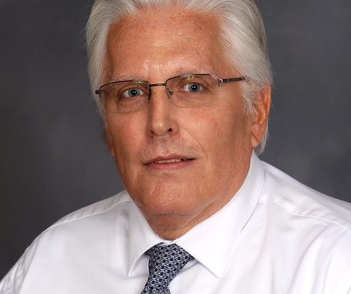 A white-haired man with glasses in a white shirt with a silver tie