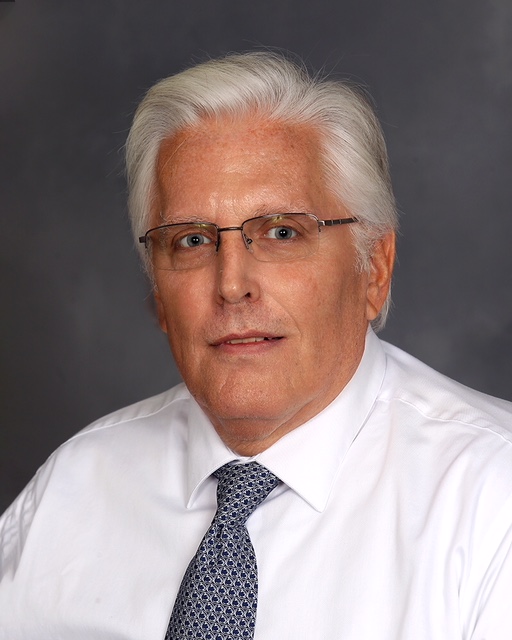 A white-haired man with glasses in a white shirt with a silver tie