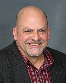 Portrait of a smiling man wearing a maroon striped shirt and dark gray jacket
