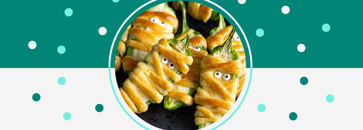 Plate of Halloween-themed mummy jalapeno poppers wrapped in strips of croissant with googly eyes