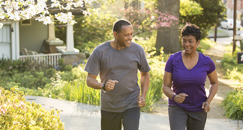 A brown-skinned man and woman in athletic clothes take a walk through a suburban neighborhood