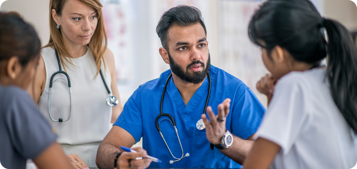 Uniformed male, medical provider is speaking directly to another provider while two others listen