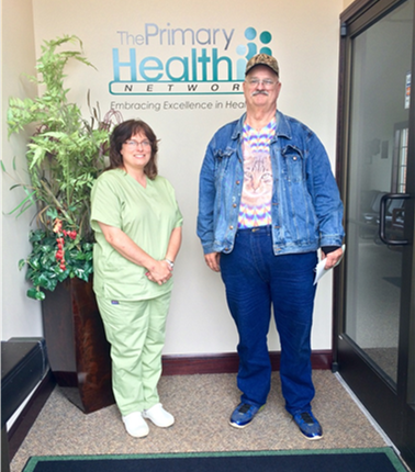 Woman in green nurse scrubs and Robert King, an older man, stand together in a PHN facility