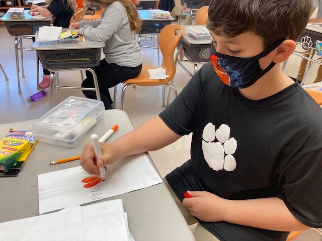 A child wearing a black shirt draws a red heart on a piece of paper