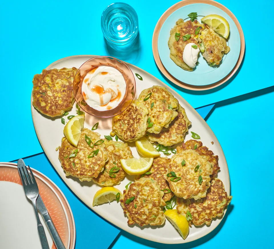 Oval platter with many circular, fried tuna fritters and lemon wedges. It sits on a blue background.