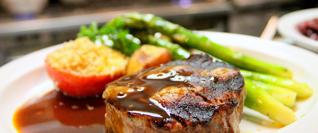 A steak with asparagus and potatoes covered in sauce