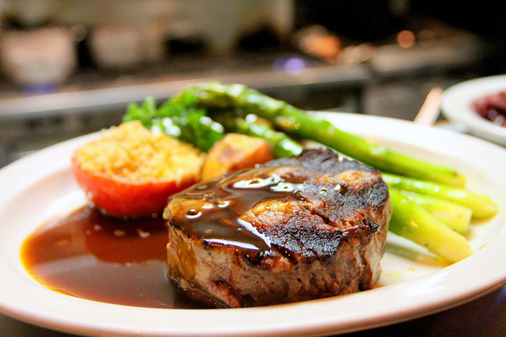 A steak with asparagus and potatoes covered in sauce