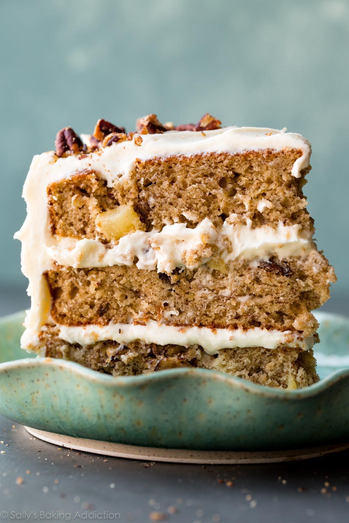 Close-up of a three-tiered hummingbird cake with white frosting and pecan pieces on a blue plate