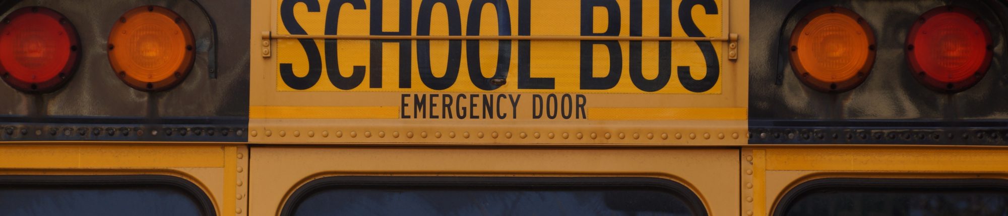 Close view: back of a yellow school bus with "school bus emergency door" at the top of the door