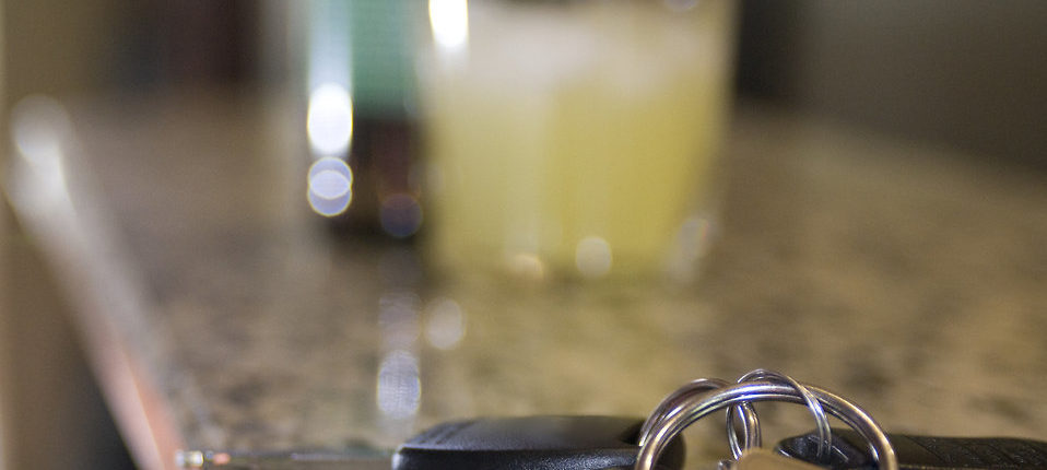 An extreme close-up of car keys on a granite countertop. Two beverages are in the background.