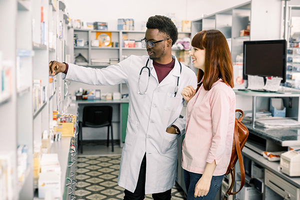 Male pharmacist is standing next to female patient behind counter, pointing at prescription