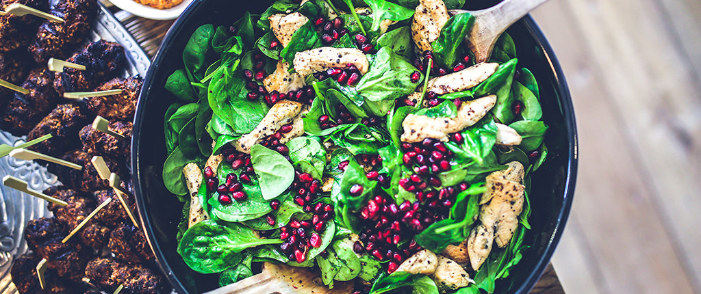 Top-down view of spinach, chicken and pomegranate seed salad next to a platter of appetizers